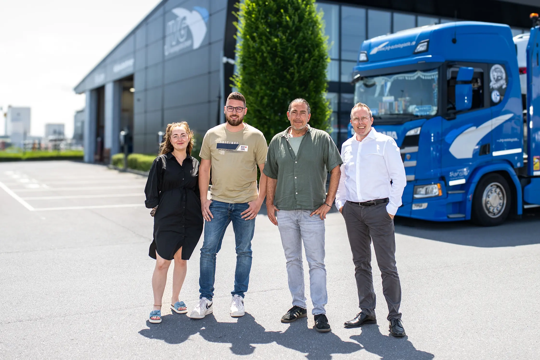 Geschäftsführer Michael Jost (rechts) steht mit drei Mitarbeitern vor dem JVG Firmengebäude. Ein blauer Scania Lkw ist im Hintergrund sichtbar.